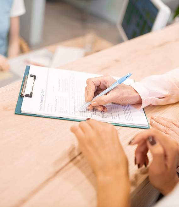 Dental team member showing a patient where to sign on a clipboard with paperwork