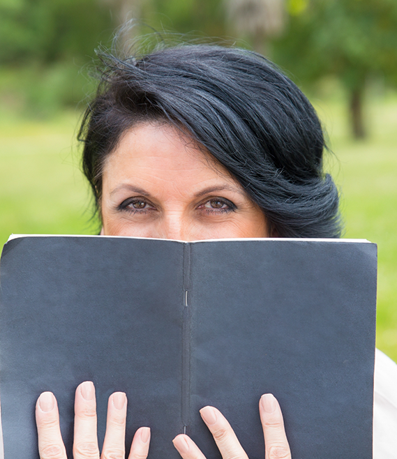 Woman holding a black notebook in front of the lower half of her face