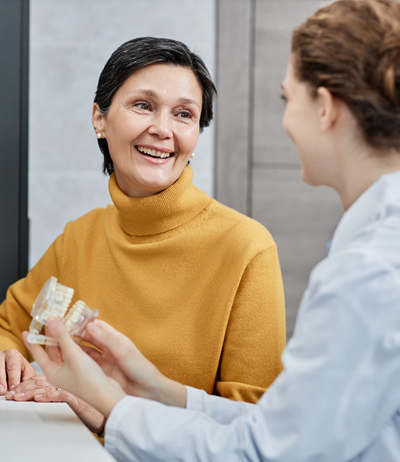 Dental team member holding a model of the teeth while talking to a senior woman