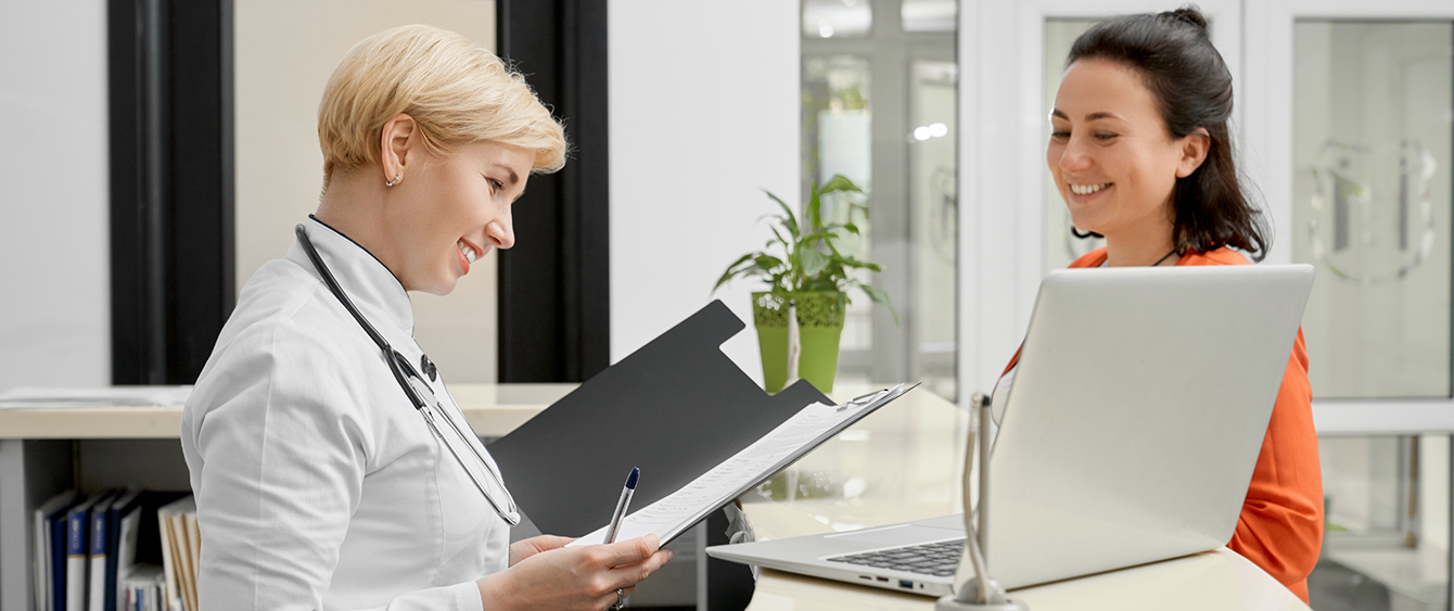 Woman holding and looking at a clipboard while talking to a receptionist