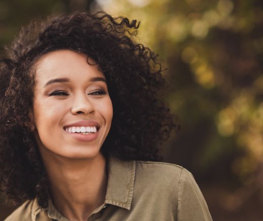 Woman in light brown collared shirt smiling outdoors