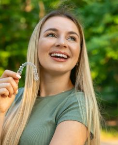 Smiling blonde woman holding an Invisalign clear aligner