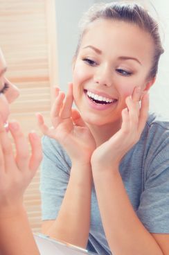 Smiling woman touching her face while looking in mirror