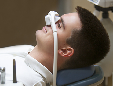 Man relaxing in dental chair with nitrous oxide mask over his nose