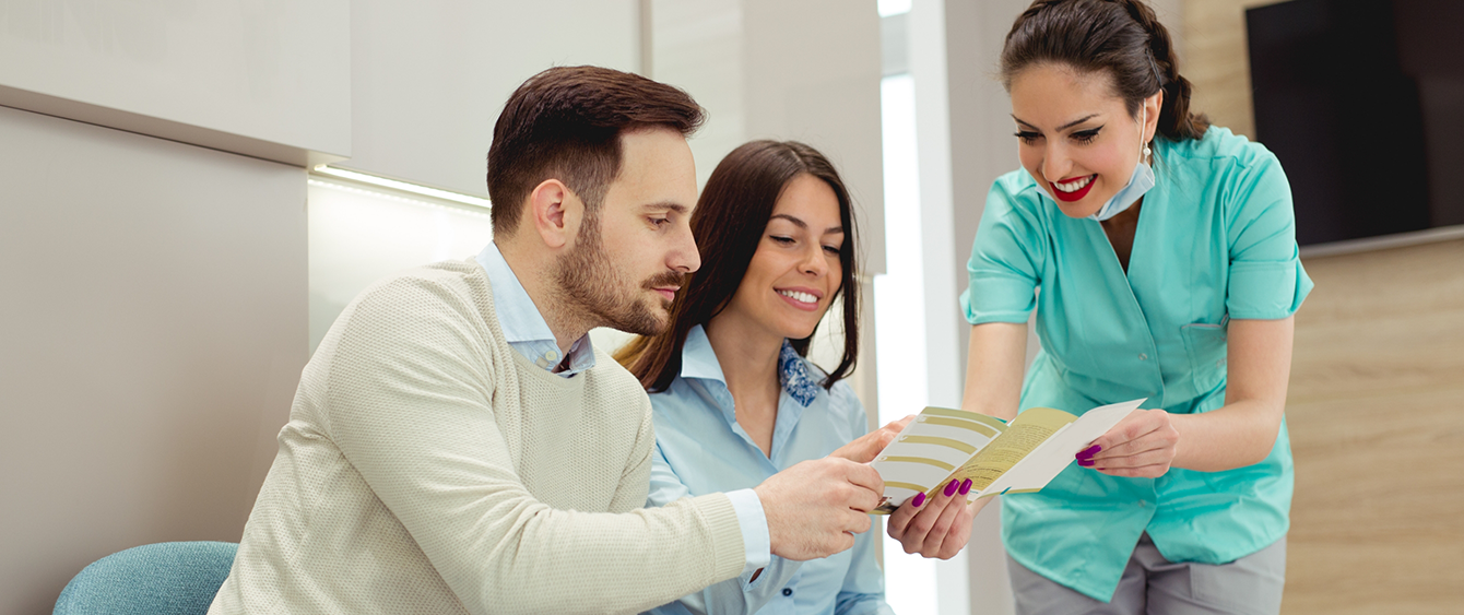 Dental team member showing a pamphlet to two patients