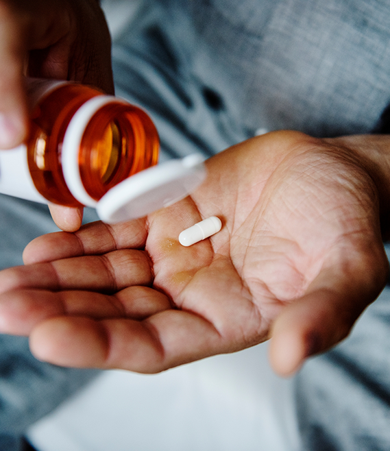 Person taking a white pill out of an orange bottle