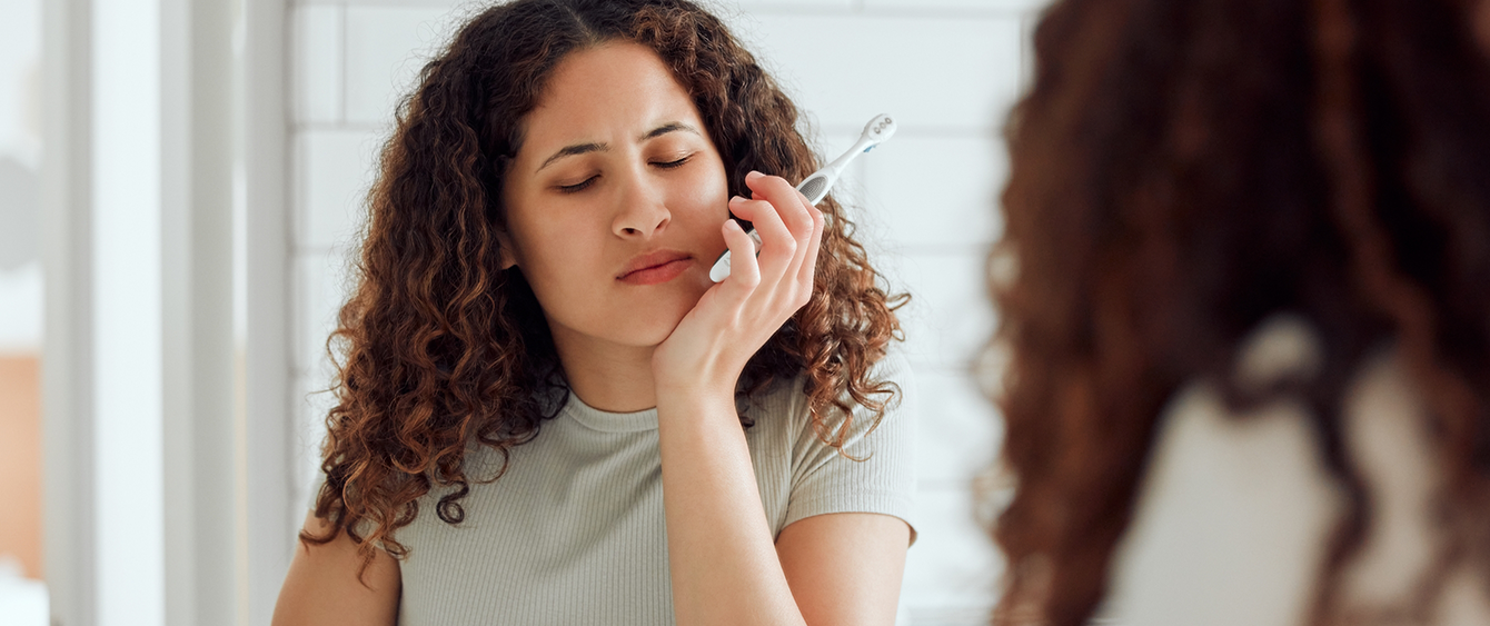 Woman holding a toothbrush and touching her jaw in pain before T M J treatment